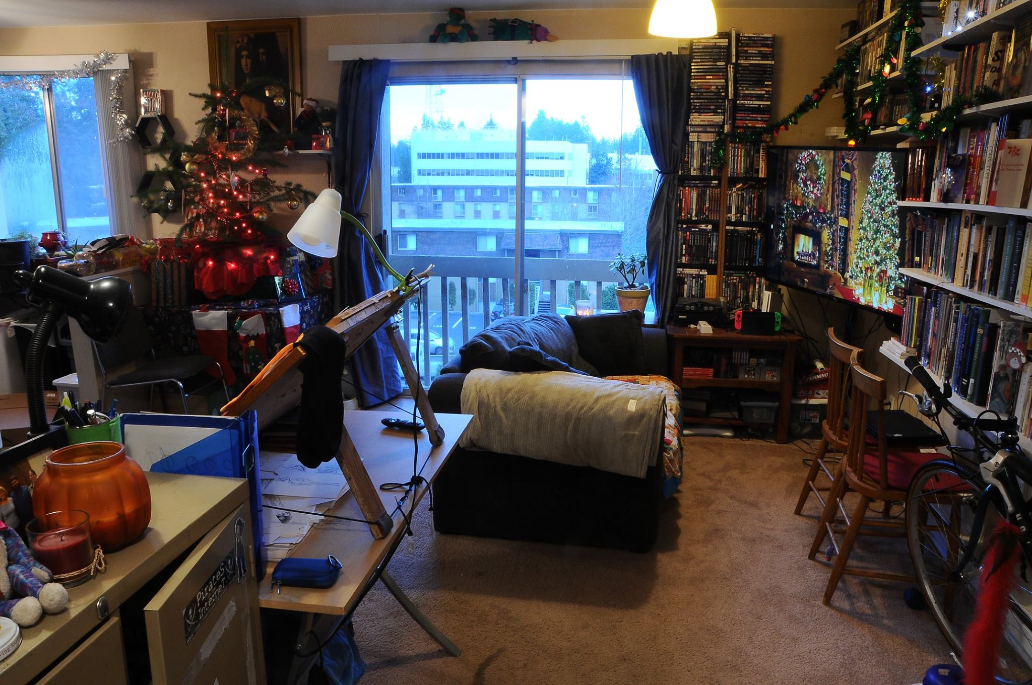 Living room in 2018. A sparse christmas tree to the left of frame. A home made easel for Morrie to draw on. The CRT has been replaced with aN LCD television, and the bean bag with a loveseat that barefly fits in the middle of the room.